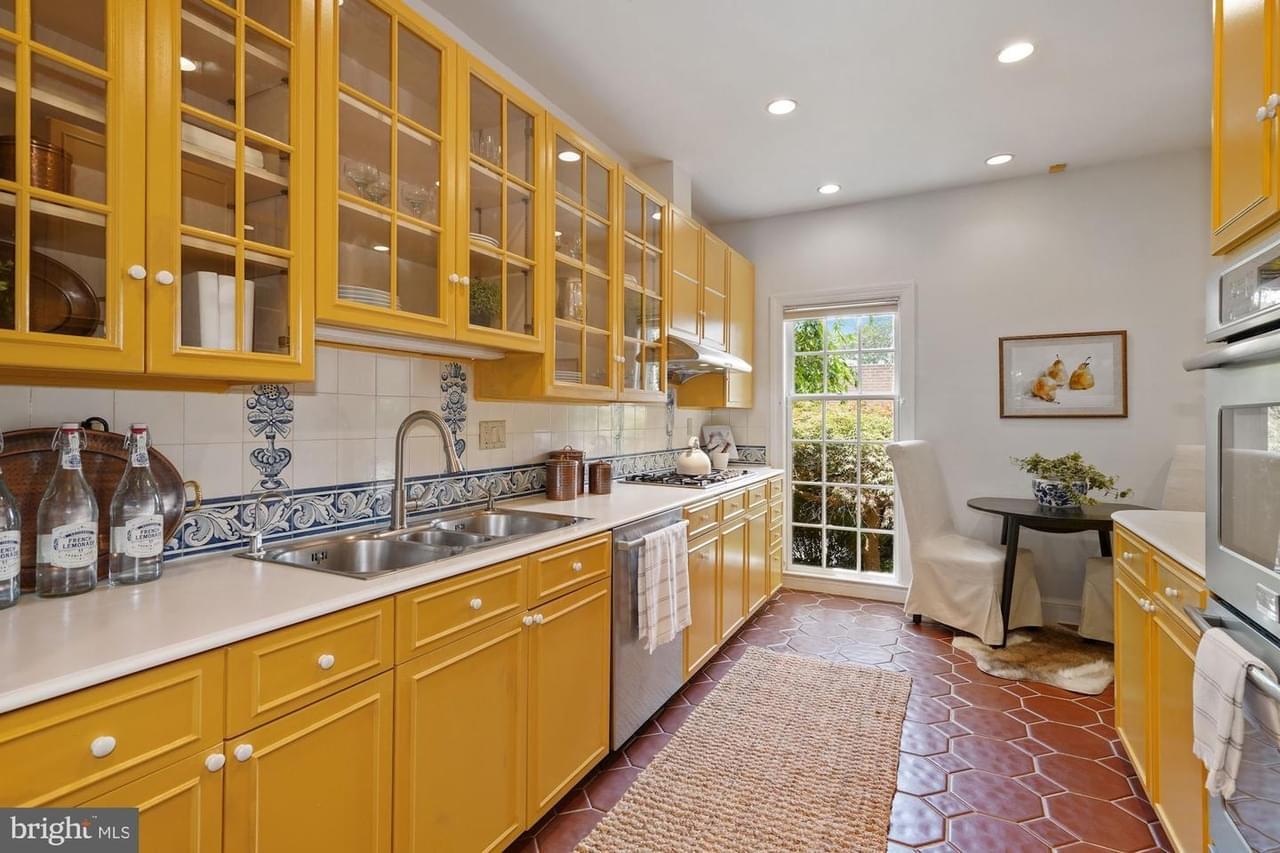 A luxury kitchen witih yellow, glass-fronted cabinetry, brick red hex tile floors, stainless appliances